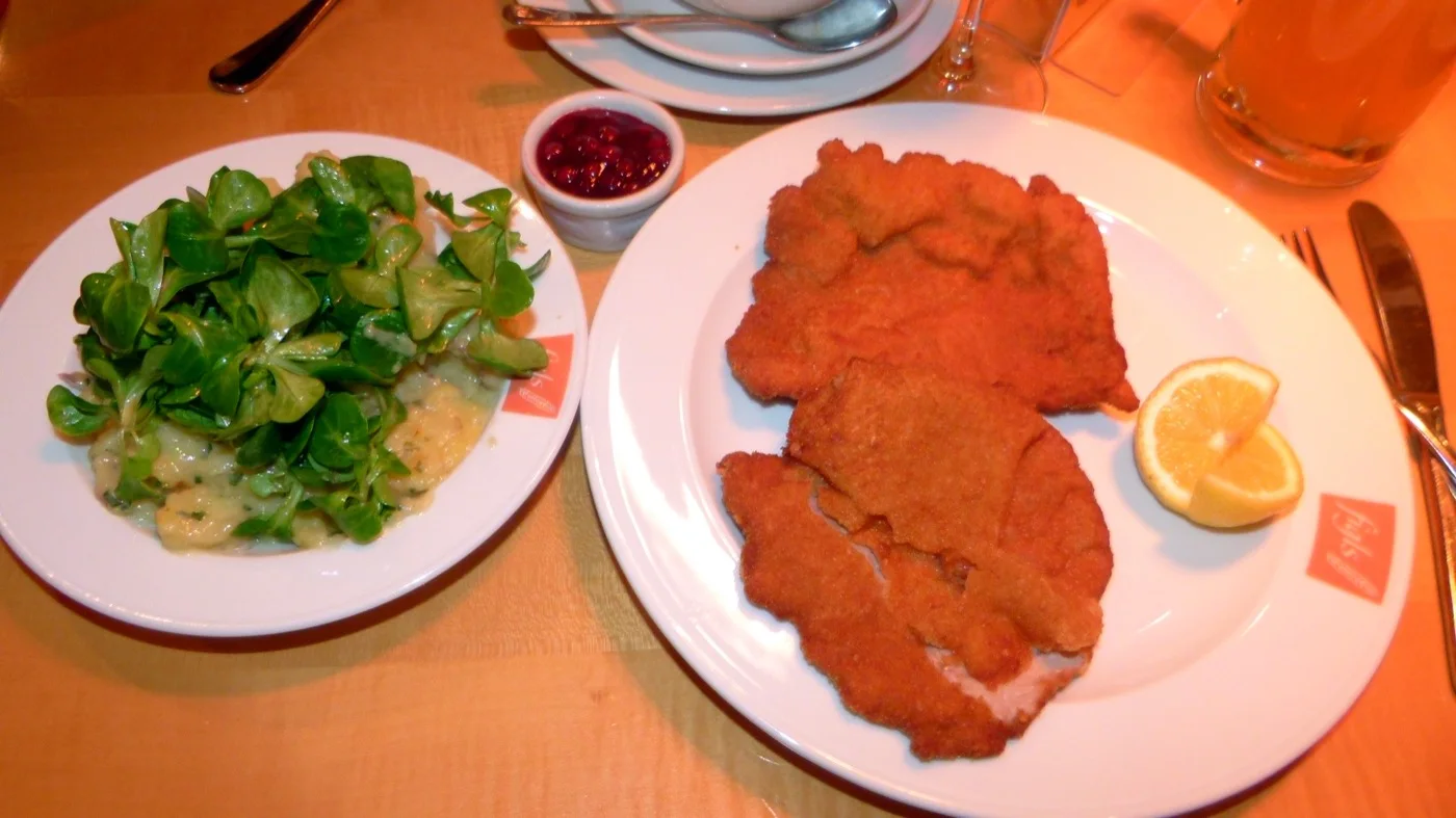 Wiener Schnitzel mit Erdäpfel-Vogerlsalat, Preiselbeeren und einem Krügerl Bier auf einem gedeckten Tisch