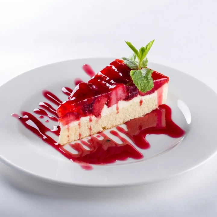 Stück Käsekuchen mit Beerenspiegel auf weißem Teller