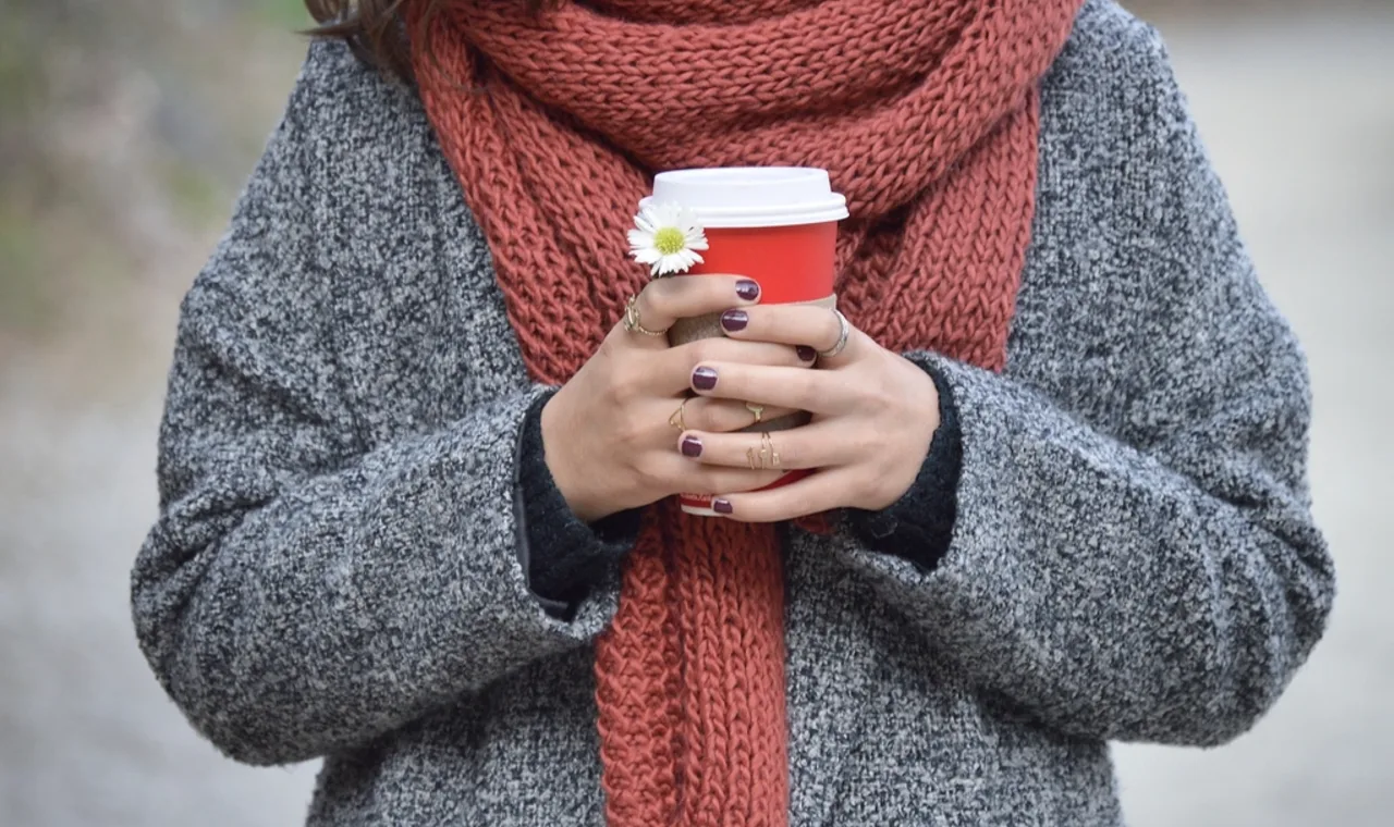 Person mit warmem Schal hält einen Coffee-to-go-Becher in beiden Händen