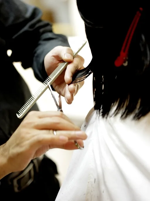 Friseurin schneidet das Haar einer Kundin mit der Schere, weißer Umhang im hellen Atelier