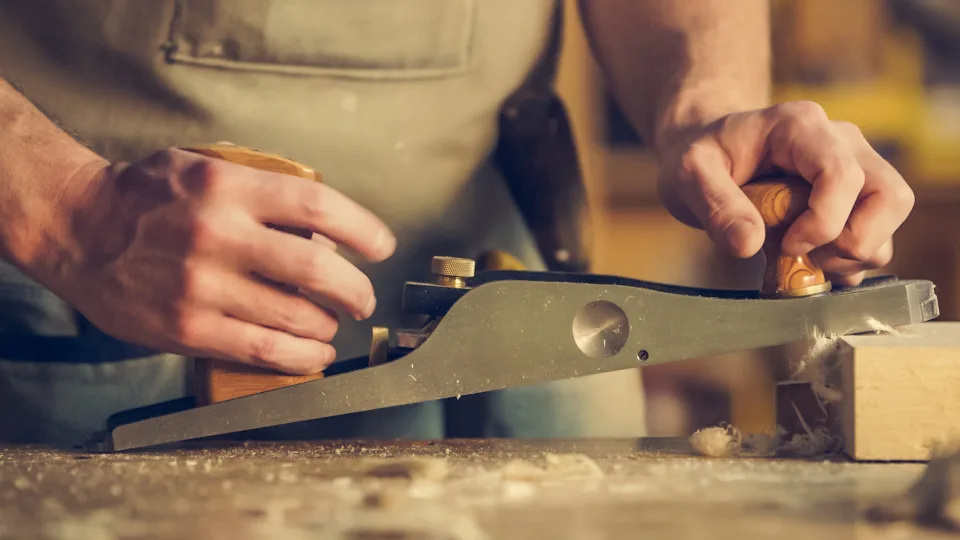 Hände hobeln mit einem Handhobel ein Werkstück, Hobelspäne fliegen.
